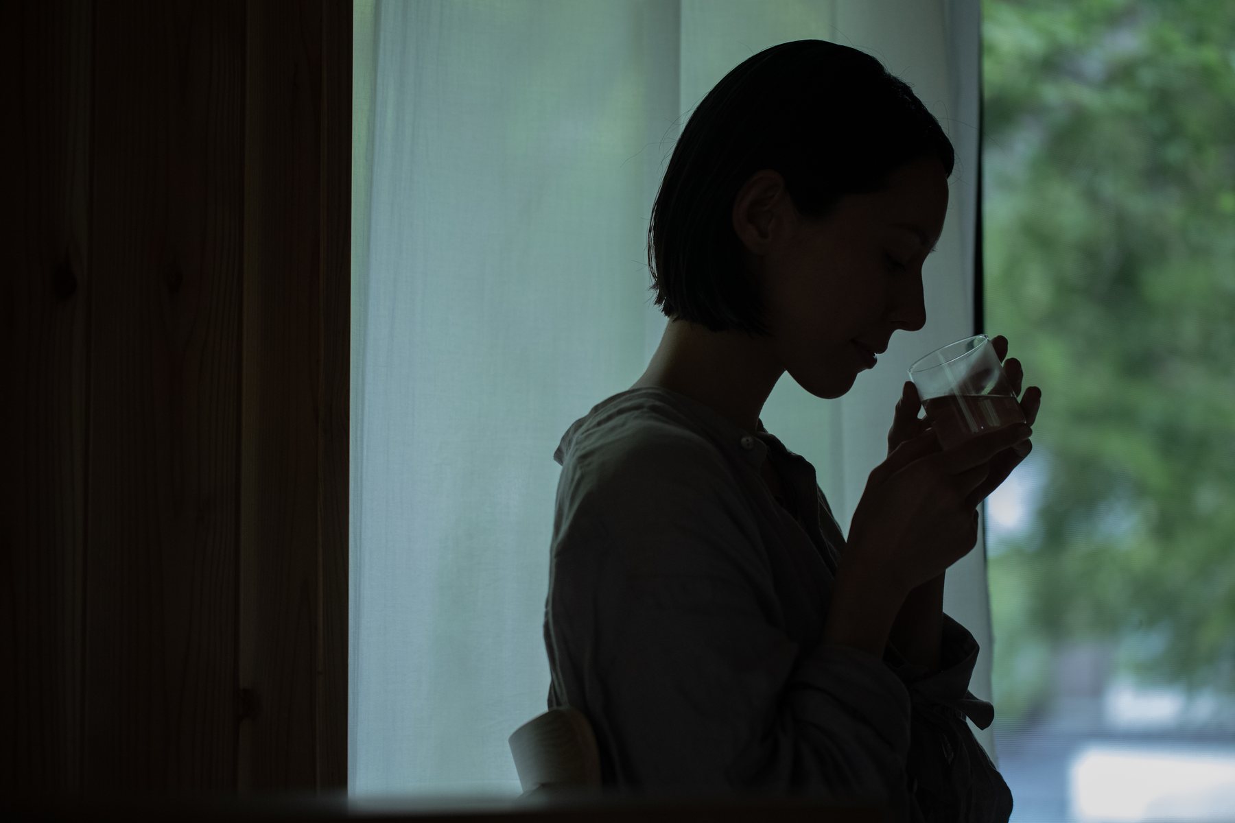 窓辺で湯気の立つカップを持つ女性